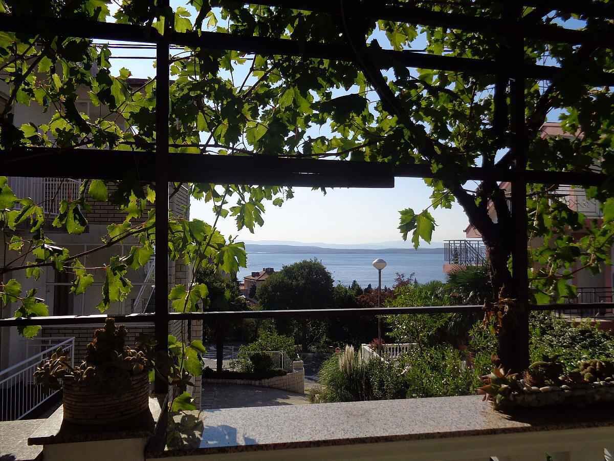 A balcony with a view of the sea, a pergola, and a stone planter.