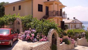 Un edificio de dos pisos con un balcón, rodeado de arcos de piedra y plantas en flor.