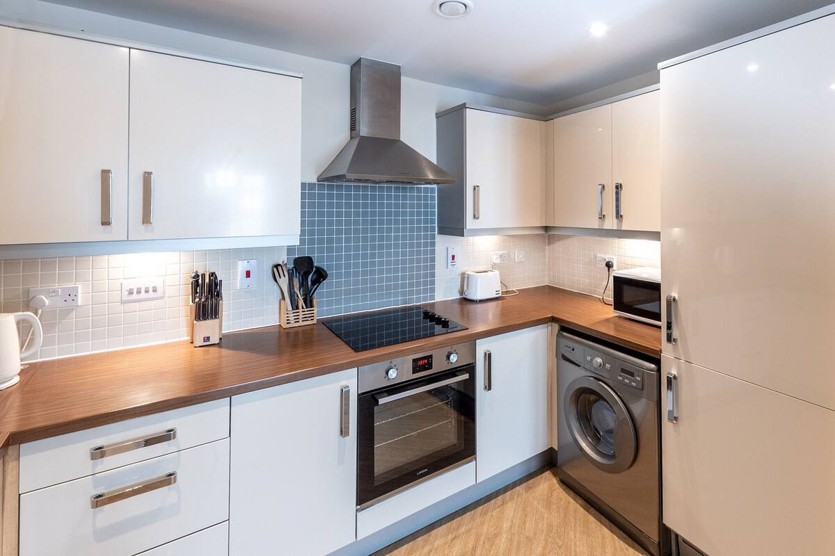 A modern kitchen with white cabinets, a built-in oven, a microwave, and a washing machine.