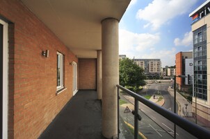Un balcón con un muro de ladrillo, un pilar de hormigón y vistas a una carretera con una glorieta.