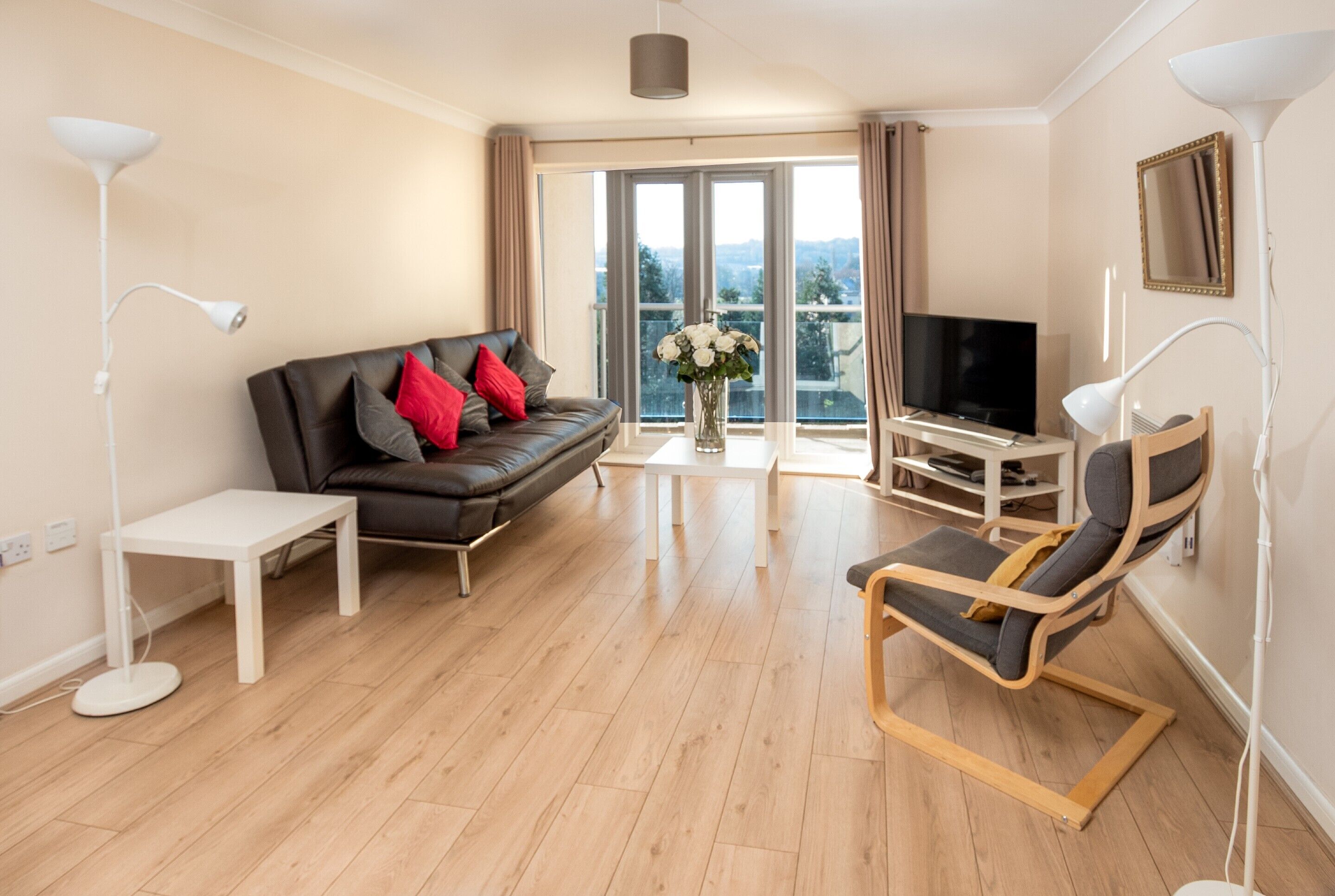 A modern living room with a sofa, a chair, a TV, and a balcony with a view.