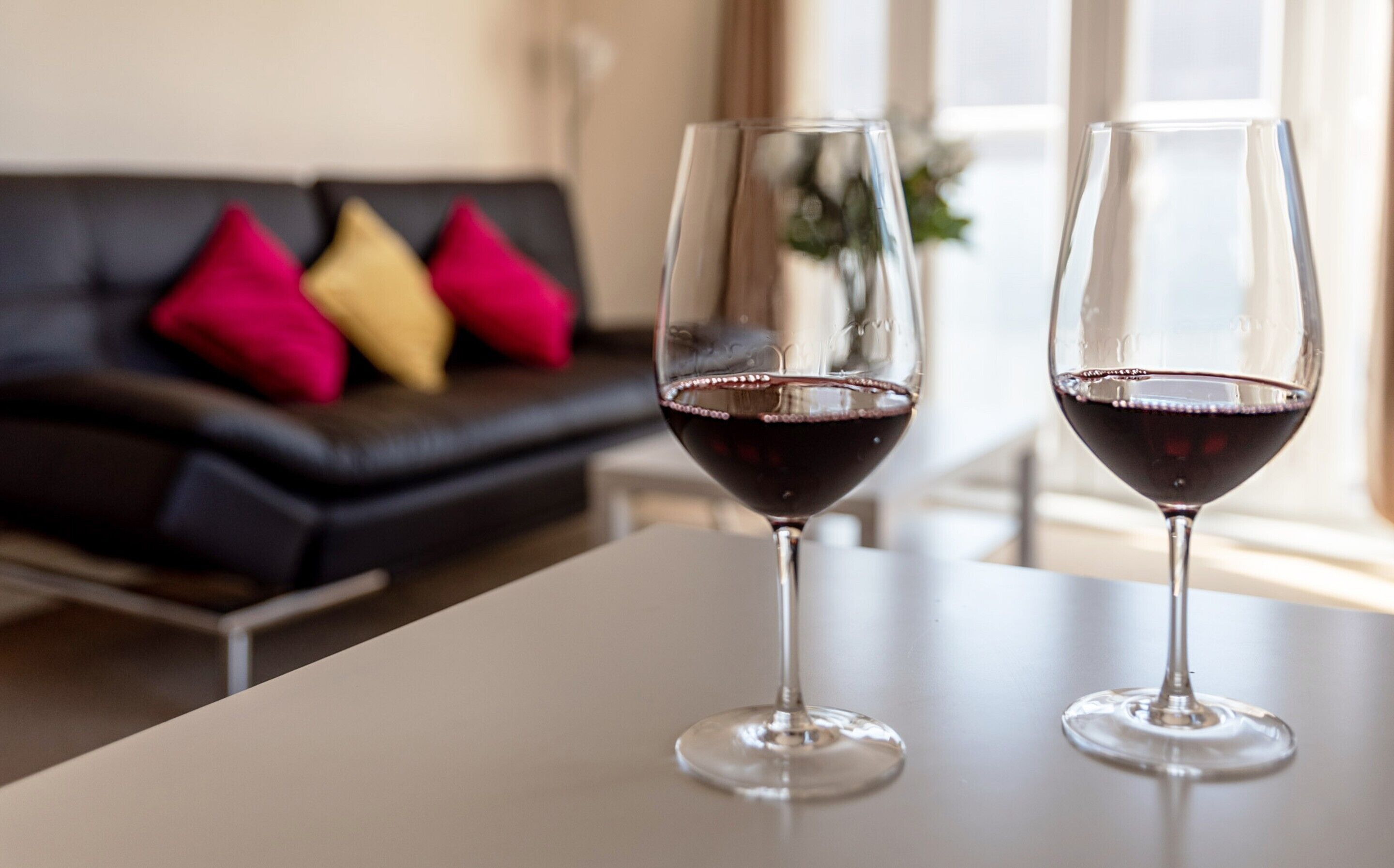 Dos copas de vino sobre una mesa, con un sofá de cuero negro al fondo.