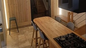 A modern kitchen with a wooden table, chairs, a gas stove, and a television mounted on the wall.