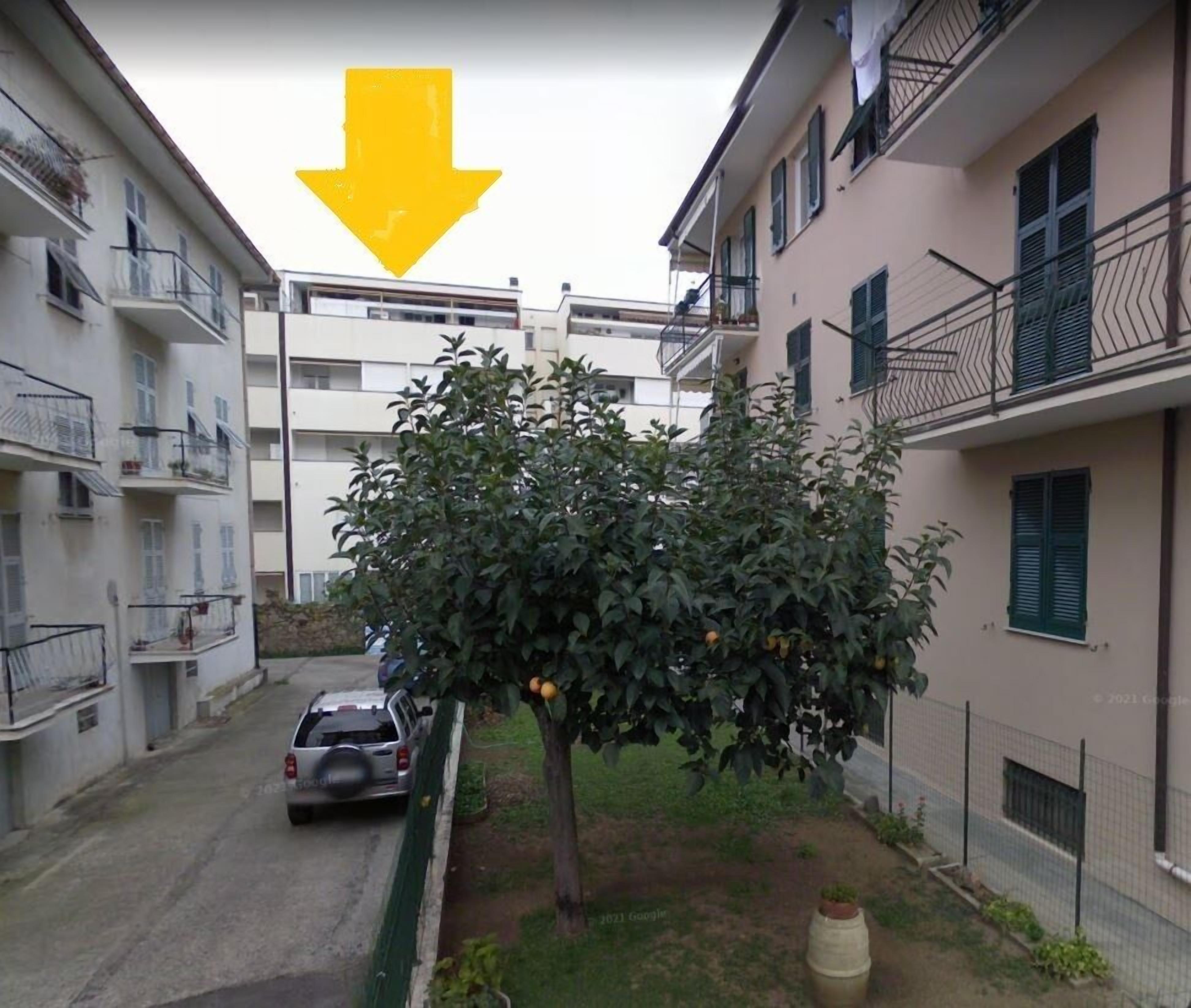 A residential area with a tree in the foreground, a parked car, and buildings with balconies.