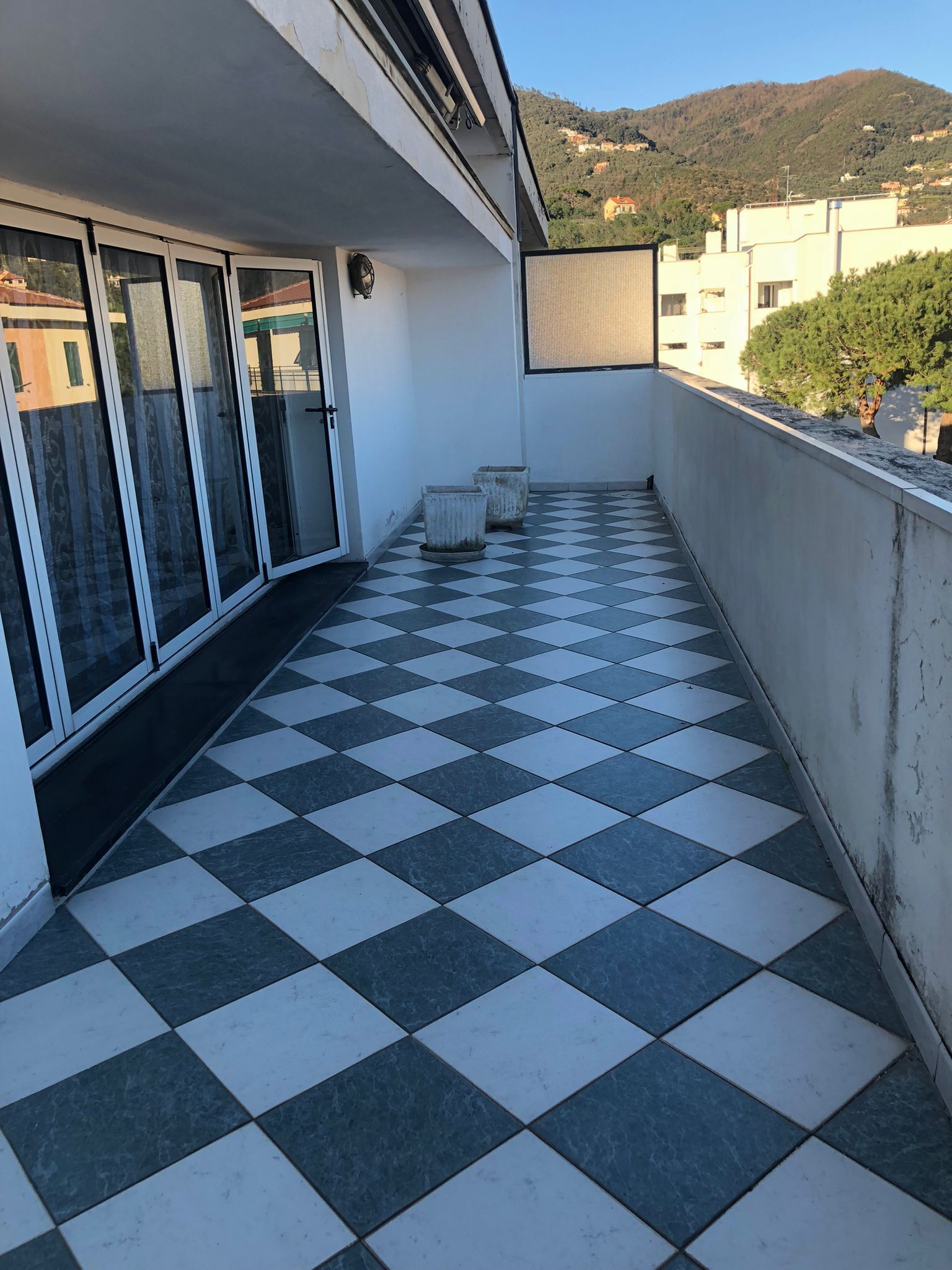 Un balcón con suelo a cuadros, ventanas amplias y vistas a una colina.