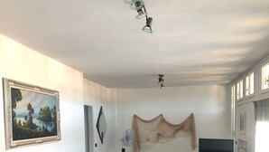 Un salon avec un canapé d’angle bleu, une table basse en verre, un téléviseur à écran plat et un tableau accroché au mur.