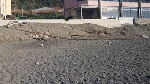 Un immeuble à plusieurs étages doté de balcons, un chantier de construction au premier plan et une colline boisée en arrière-plan.