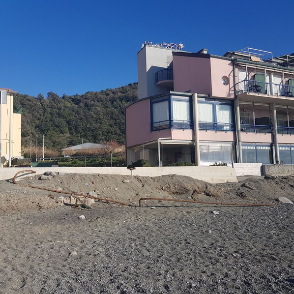 A multi-story building with balconies, a construction site in the foreground, and a forested hill in the background.