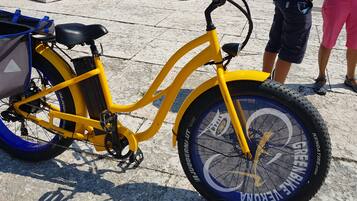 Una bicicleta amarilla con un bolso de almacenamiento y una cesta delantera, estacionada sobre una superficie pavimentada.