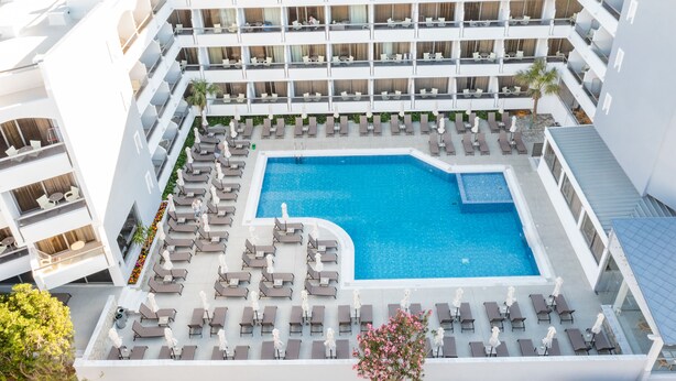 Um hotel com vários andares, com uma piscina central rodeada por espreguiçadeiras e um pequeno jardim.