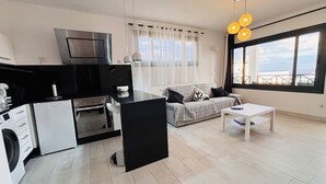 Een moderne keuken met een wasmachine, een zwart aanrecht en een groot raam met gordijnen.