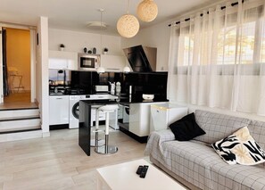 A modern kitchen with a microwave, stove, and sink, a dining area with a bar stool, and a living room with a sofa and a coffee table.