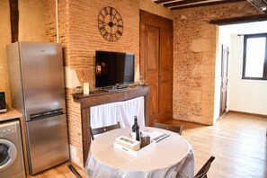 A compact kitchen with a refrigerator, a television, and a table with a bottle and glasses. - Charming 2 bedroom apartment "Cyrano" - Habitation Saint-Clar Historic Center - WIFI / Netflix (Bergerac)