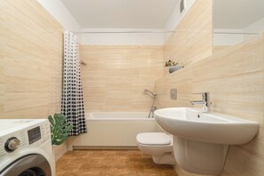 A modern bathroom with a bathtub, toilet, and washing machine.