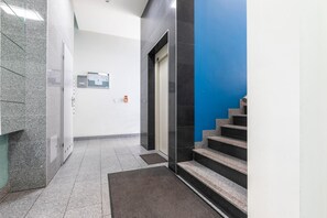 A hallway with a marble floor, a blue wall, and a staircase with a black handrail. - MARGI Brandy Apartament (Szczecin)