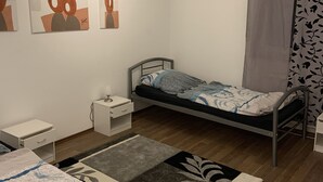 Quarto com uma cama de solteiro, mesa de cabeceira, cômoda e parede com três quadros abstratos.