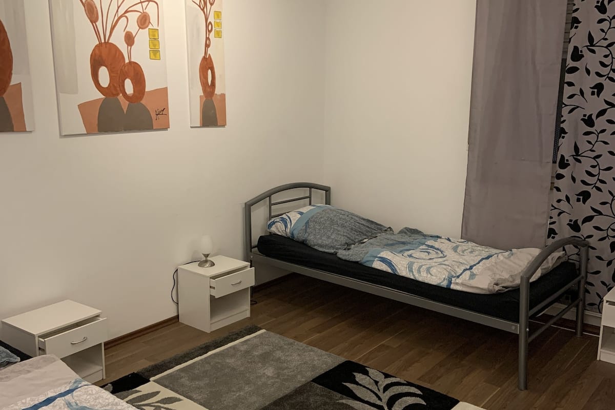 A bedroom with a single bed, a nightstand, a dresser, and a wall with three abstract paintings.