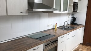 Uma cozinha moderna com armários brancos, coifa de aço inoxidável, forno embutido e bancada de madeira.
