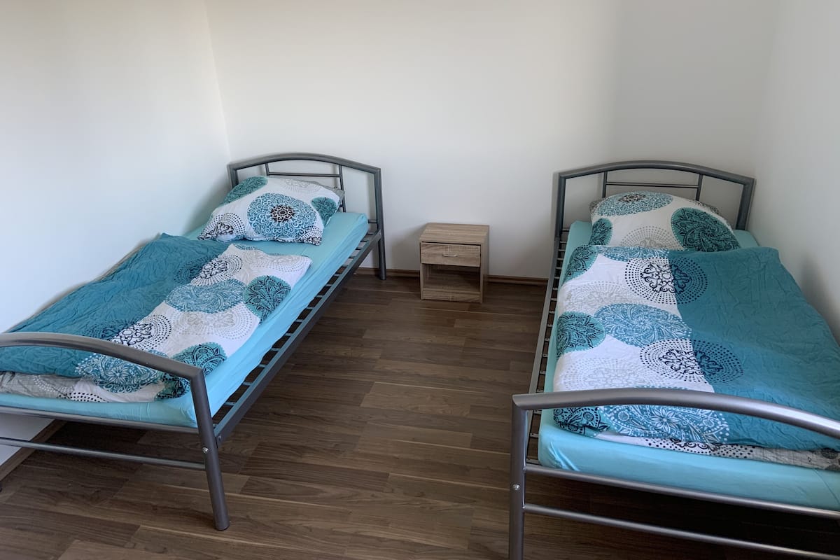 Two single beds with metal frames, a small wooden nightstand, and a plain white wall.