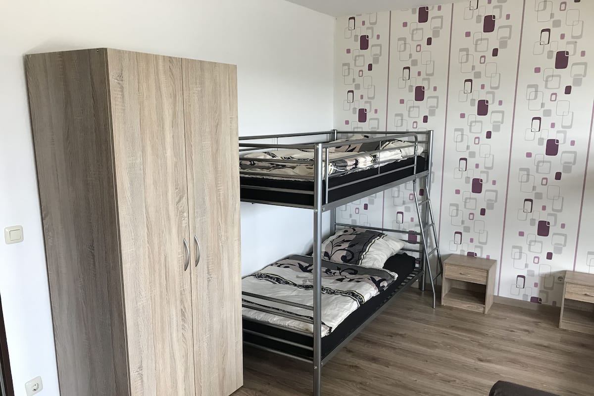 A bunk bed with a wooden wardrobe, a patterned wall, and a small wooden table.