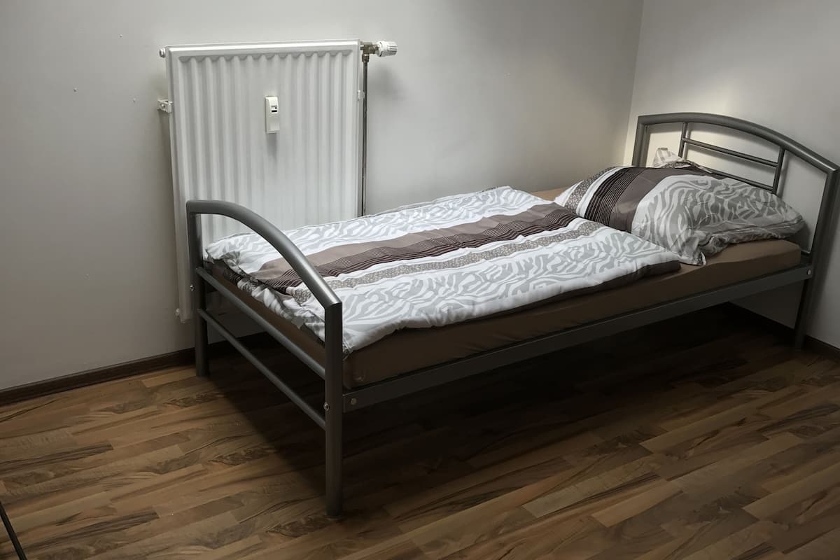 A single bed in a room with a skylight, wooden flooring, and a radiator.