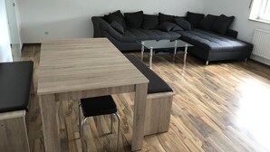 Uma sala de estar moderna com mesa de jantar de madeira, cadeiras estofadas pretas, mesa de centro de vidro e sofá seccional cinza escuro.