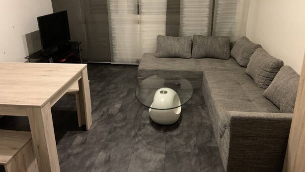 Uma sala de estar moderna com uma mesa de centro de vidro, sofá cinza e uma mesa de madeira.