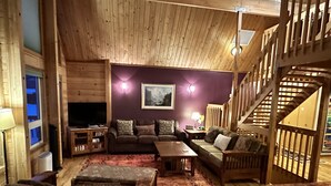 A cozy living room with wooden furniture, a flat-screen TV, and a staircase.