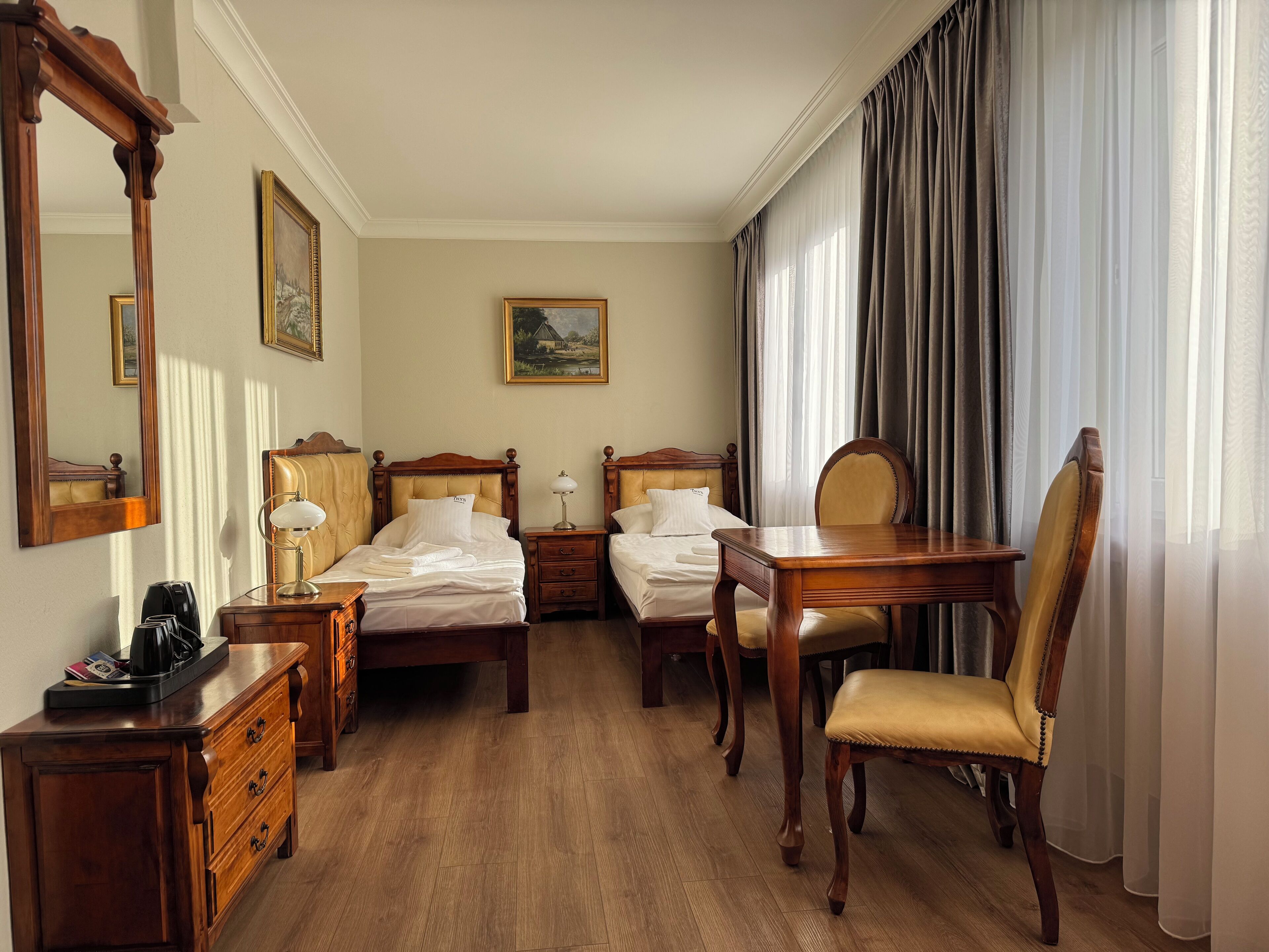 A hotel room with two wooden beds, a wooden desk, a chair, a dresser, and a large mirror.