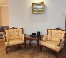 Deux fauteuils à l’accoudoir, dotés d’un revêtement capitonné et de cadres en bois, une petite table en bois avec une machine à café, et un tableau représentant un paysage, encadré et accroché au mur.