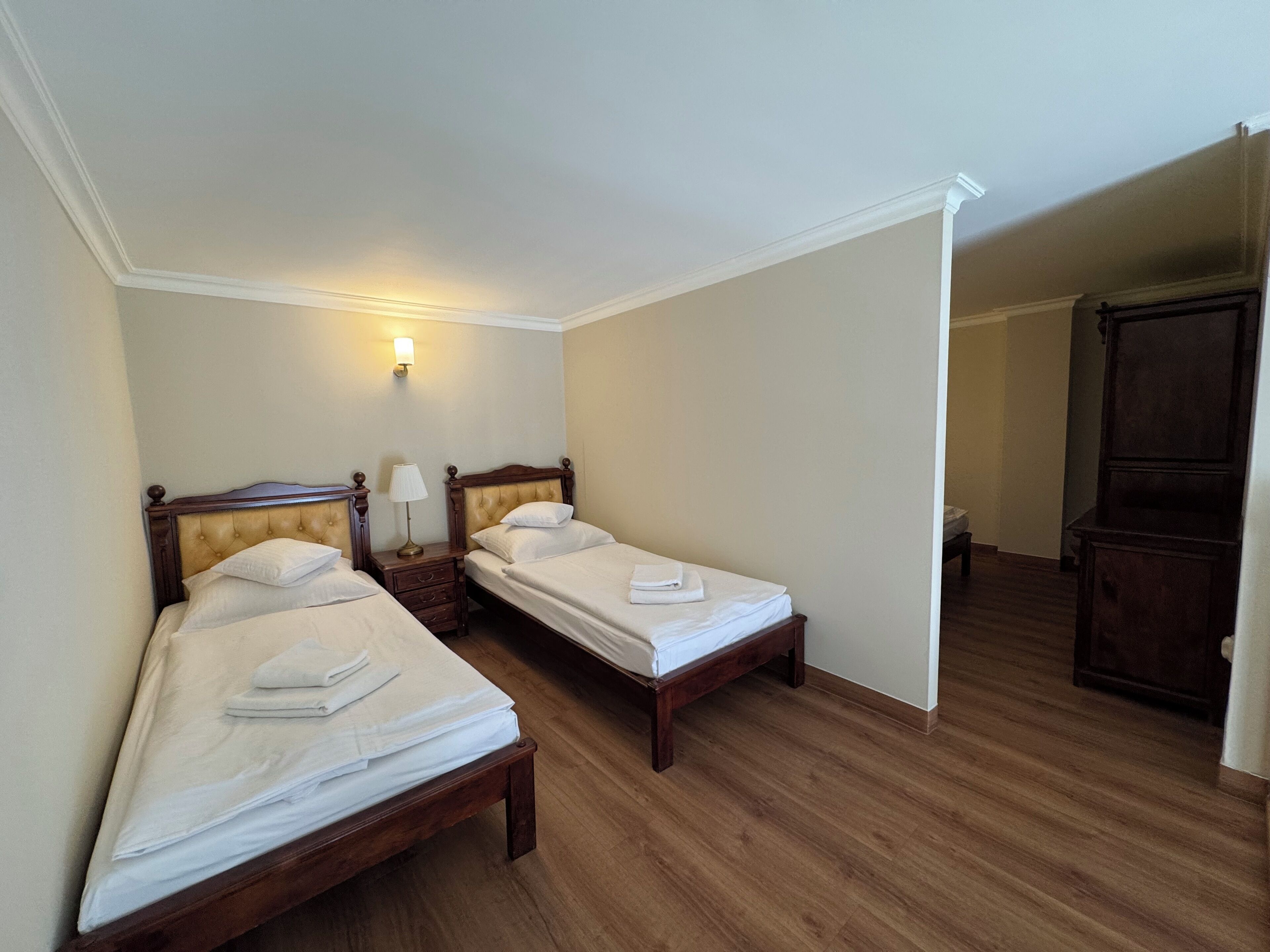 Een hotelkamer met twee eenpersoonsbedden, houten hoofdeinden, een nachtkastje met een lamp en een garderobe.