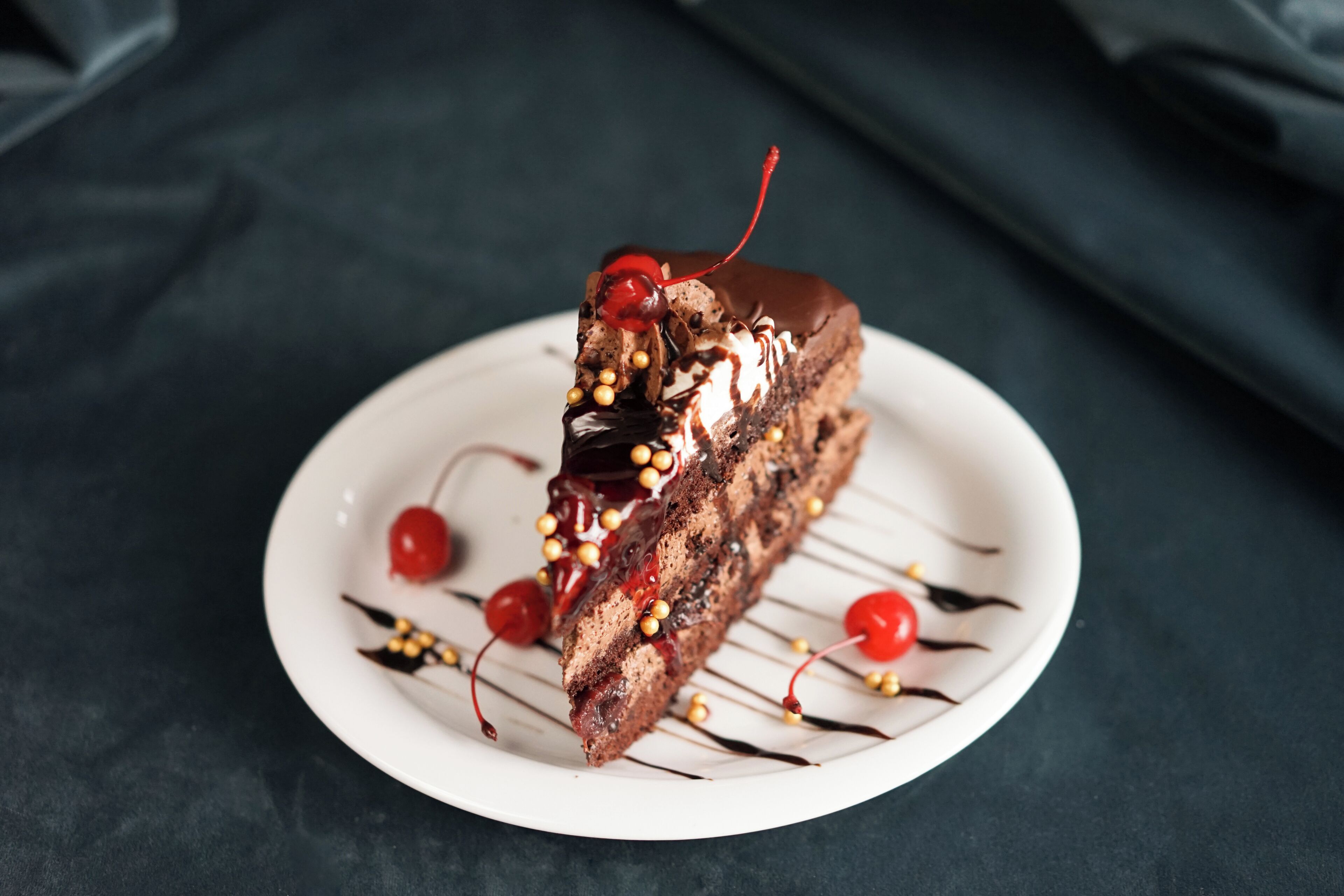 Un postre en un plato blanco con cerezas y un hilo de chocolate.