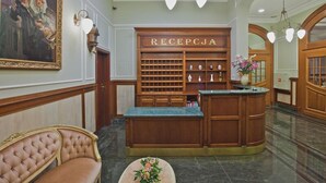 Zona de recepción con un mostrador de madera, un área de descanso con un banco acolchado y un cuadro colgado en la pared.