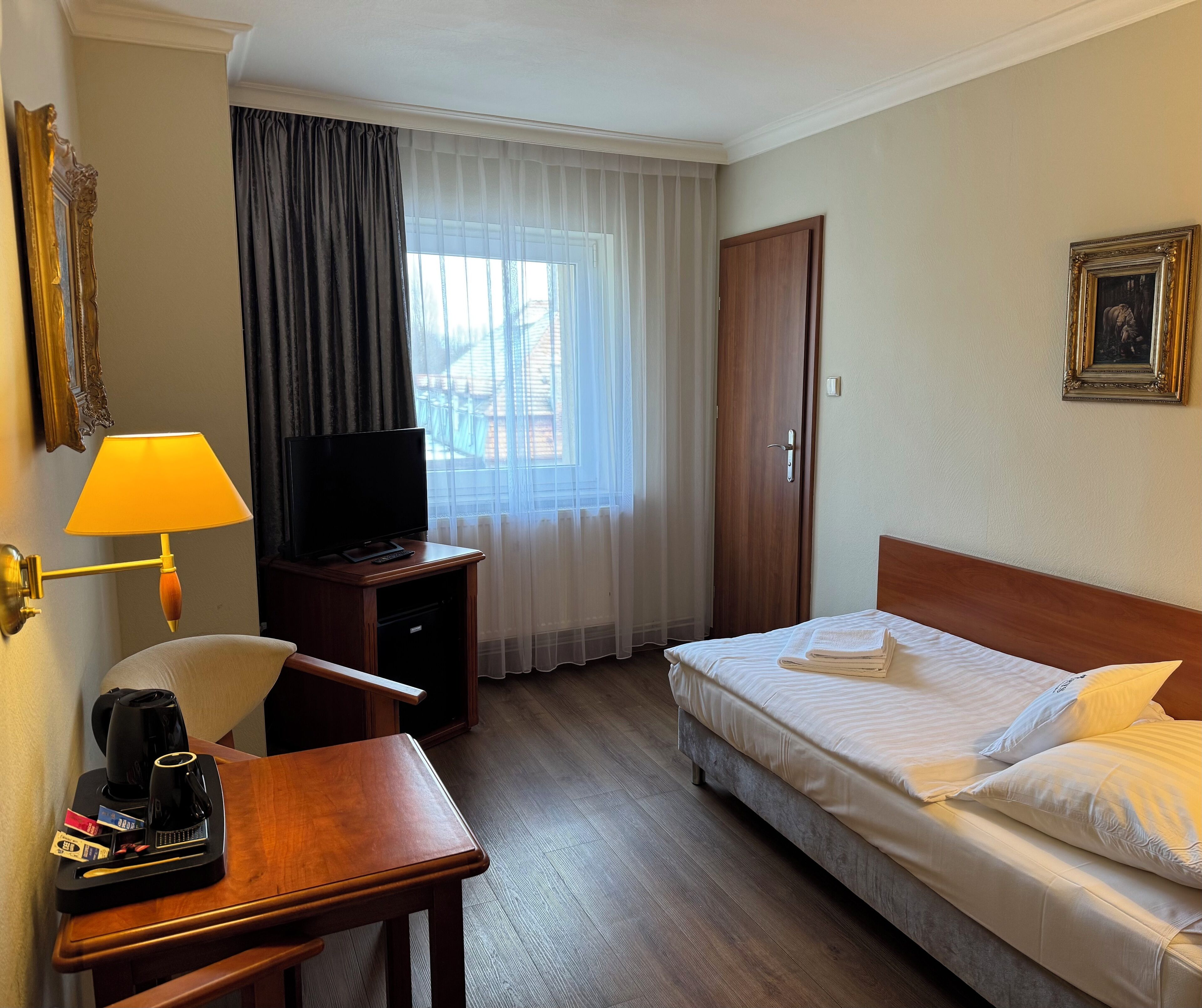 A hotel room with a bed, a desk with a lamp, a television, and a coffee maker.