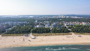 Vista aérea de una ciudad costera con playa, edificios y una zona boscosa.