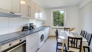 A modern kitchen with a built-in washing machine, a coffee maker, and a dining area with a table and chairs. - Stay Here ND Apartments (Krefeld)