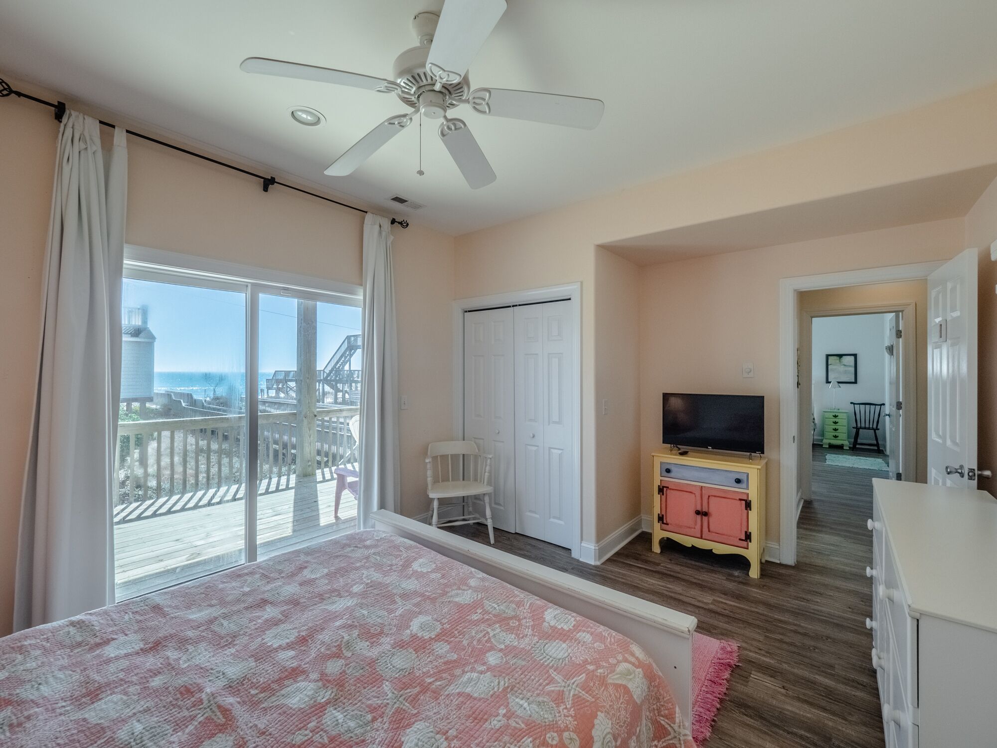 A bedroom with a bed, a television on a cabinet, and a balcony with a view of the beach.