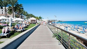Een promenade aan het strand met ligbedden, palmbomen en een helderblauwe lucht.