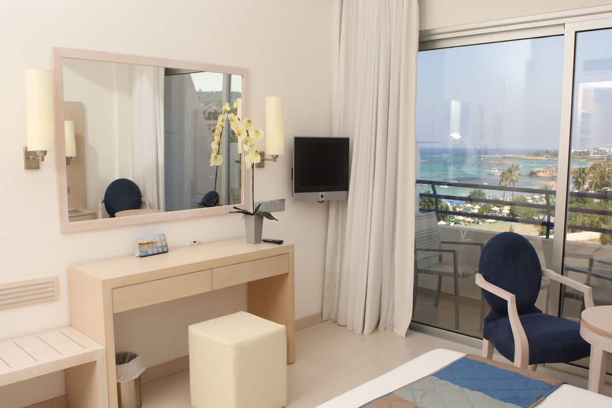 Habitación de hotel con un espejo grande, un televisor de pantalla plana, un escritorio con una silla, un pequeño reposapiés y vistas al mar.