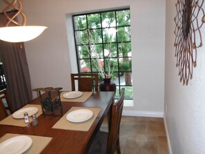 A dining room with a wooden table set for four, a window with a view of greenery, and a decorative wall piece.