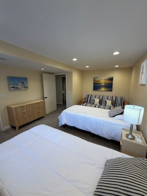A hotel room with a bed, a bedside table with a lamp, a wooden dresser, and artwork on the walls.