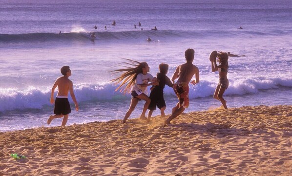 A sandy beach with people running and playing in the sand.