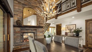 A dining area with a stone fireplace, wooden ceiling, and a chandelier.