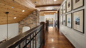 A wooden interior with a staircase, stone wall, and framed pictures on the wall.