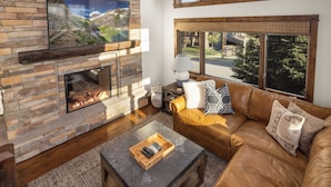 A living room with a stone fireplace, leather sofa, and a TV mounted on the wall.