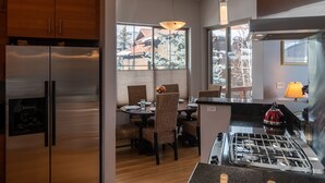 Une cuisine moderne dotée d’appareils électroménagers en acier inoxydable, un coin repas avec des chaises en osier et de grandes fenêtres offrant une vue sur l’extérieur.