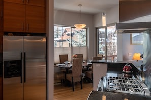 A modern kitchen with stainless steel appliances, a dining area with wicker chairs, and large windows offering a view of the outside. - Locally designed town home has been crafted with traditional JH in mind! (Jackson)