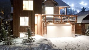 Une maison en bois à deux étages, dotée d’un garage, entourée d’un paysage enneigé et d’arbres.