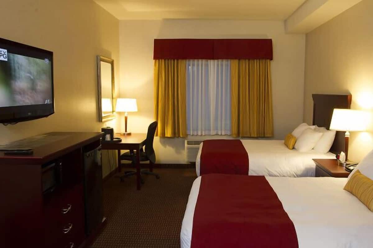 Habitación de hotel con televisión, escritorio con silla, dos camas y ventana con cortinas.