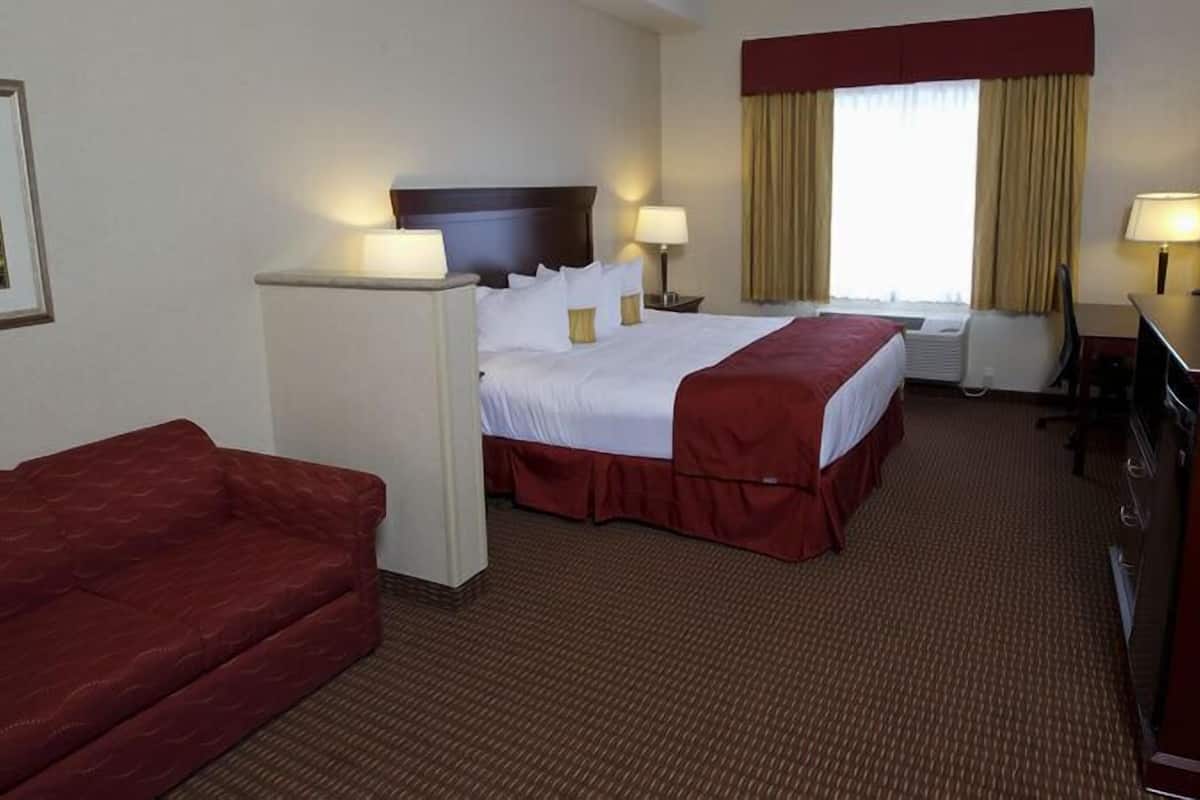 Habitación de hotel con cama, dos mesitas de noche, escritorio, silla, sofá rojo y ventana grande con cortinas.